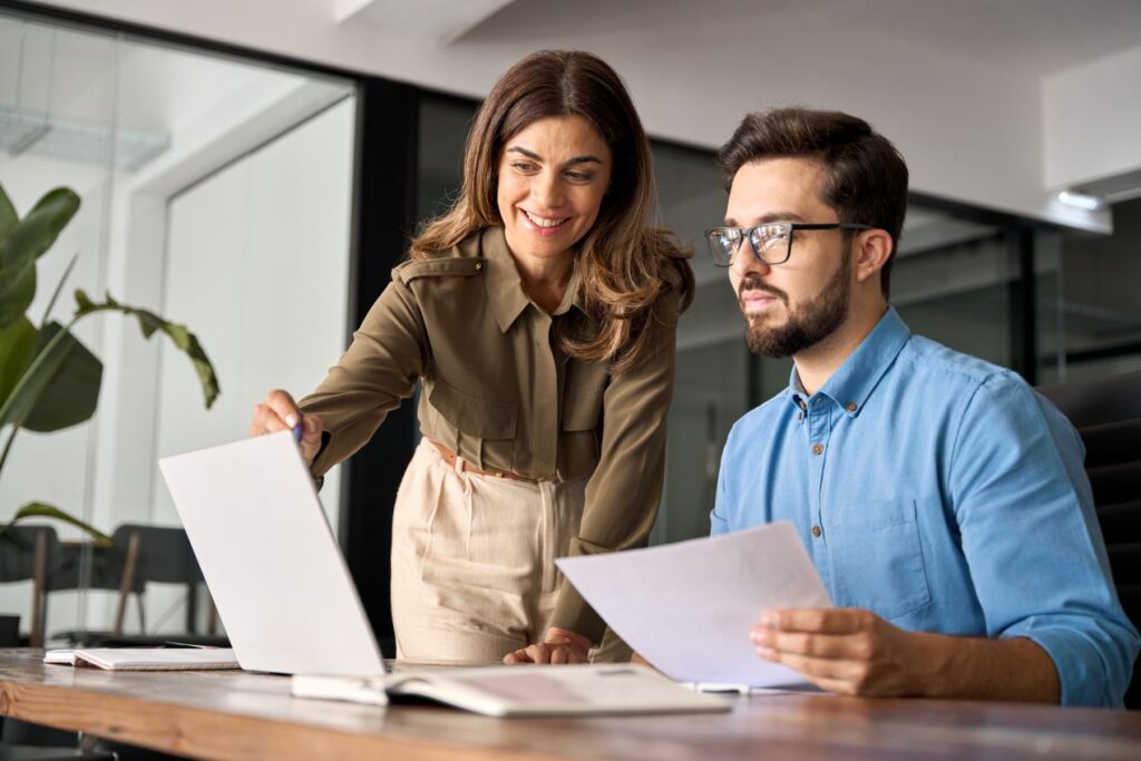 Eine Frau erklärt einem Kollegen Inhalte auf einem Laptop. Unternehmen profitieren von E-Learning Anbietern, die digitale Weiterbildung effizient gestalten.